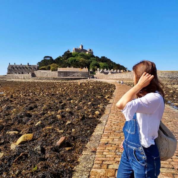 Giselle looking holding her hair, looking towards St Michael's Mount in Cornwall, from the causeway at low tide