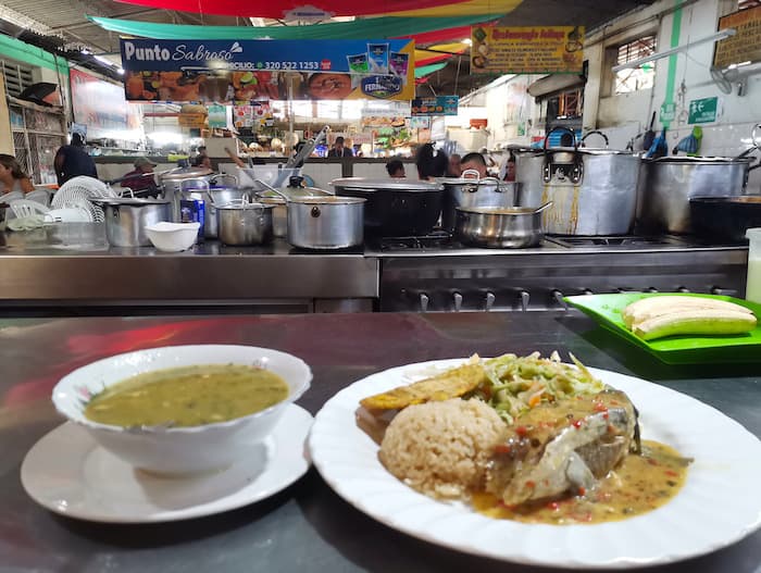 A bowl of soup and a plate of rice with fish and salad, served in La Alameda Market. Visiting La Alameda is one of the best things to do in Cali, Colombia!