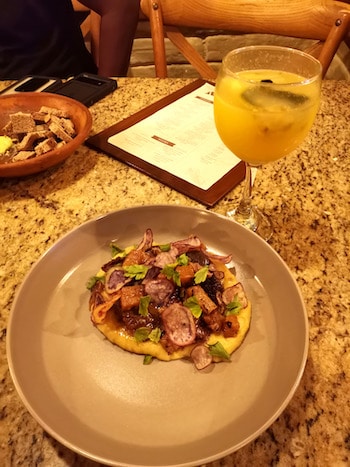 A plate of mashed potato with meat and a passion fruit cocktail