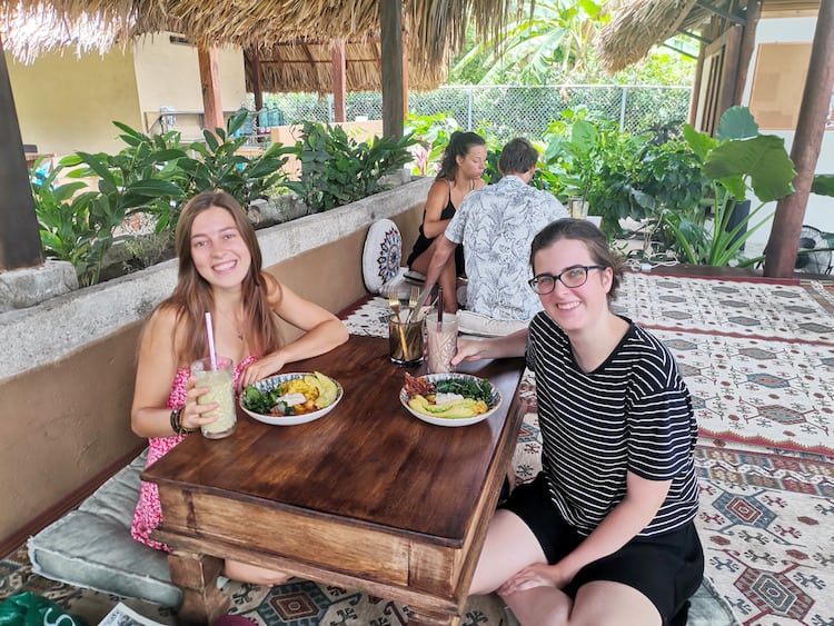 Giselle and her friend sat at a wooden table on the floor with freshly prepared breakfast and two smoothies at Cafe Holss in Palomino