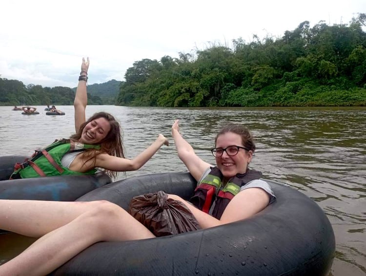 Two girls sat in big black rubber tubes with their arms out in excitement floating down a river. This is by far one of the best things to do in Palomino, Colombia!