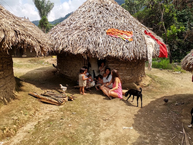 Giselle interacting with an indigenous Kogi family just outside their circular mud, stone and palm hut. Visiting an indigenous village is one of the best things to do in Palomino, Colombia!